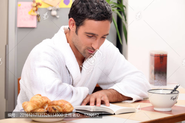 英俊的男人在早餐時讀一本書