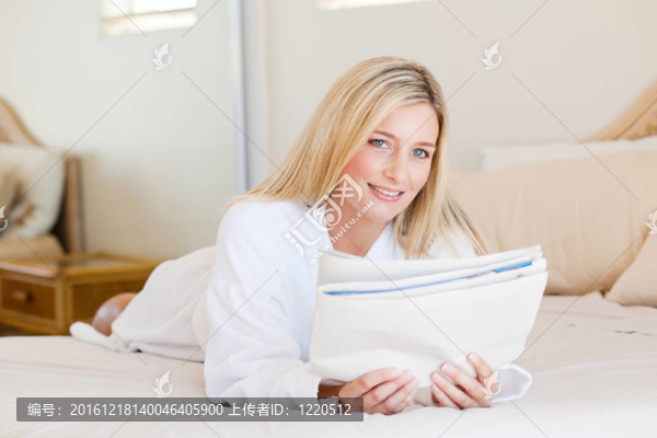 漂亮的年輕女人在床上看報紙