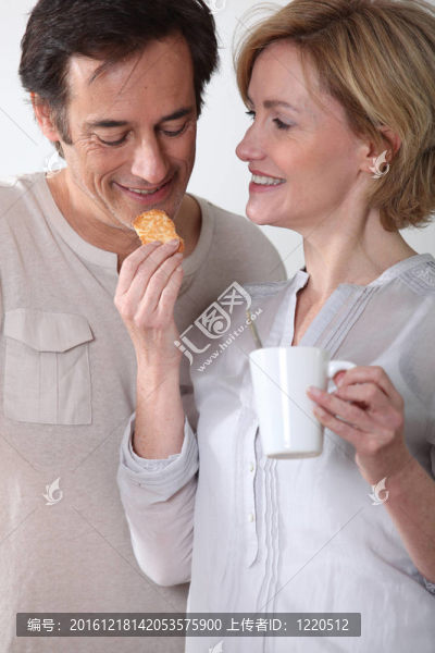 女人拿著一杯咖啡喂她的伙伴一塊餅干
