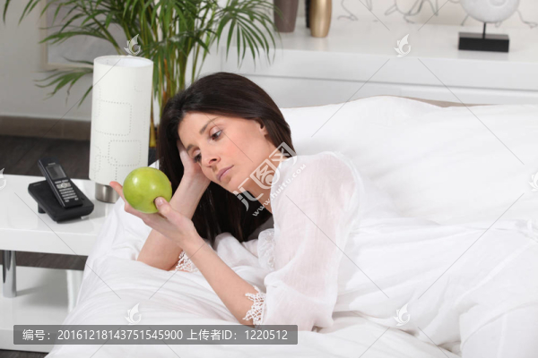 憂郁的女人在床上看一個蘋果