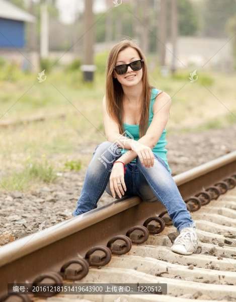 戴眼鏡的年輕女孩坐在鐵路上。