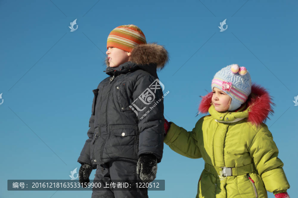 小女孩穿著一件綠色的夾克和男孩站在雪和展望了在冬季；女孩在男孩的手