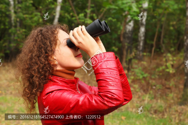 漂亮的年輕女子穿著紅色皮夾克；用雙筒望遠鏡向外看