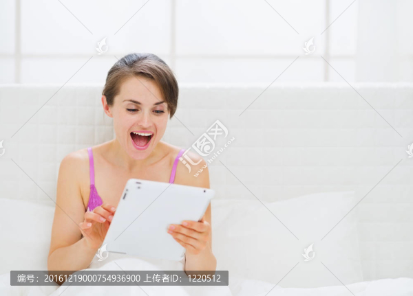 驚訝的女人坐在床上，使用平板電腦