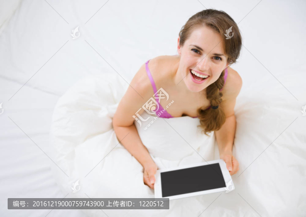 微笑的女人坐在床上，使用平板電腦