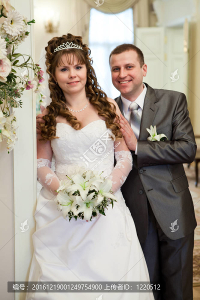 幸福的新婚夫婦站在一起的白種人。白色的衣服和灰色西裝。一串百合花