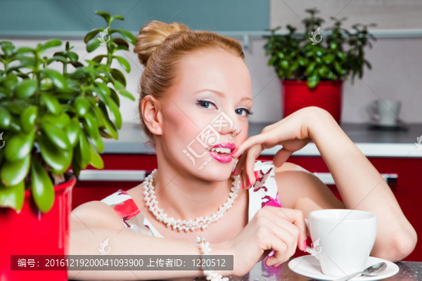 年輕漂亮的性感女孩穿著白色和粉紅色的衣服與一杯早晨咖啡在紅色現(xiàn)代廚房內(nèi)部