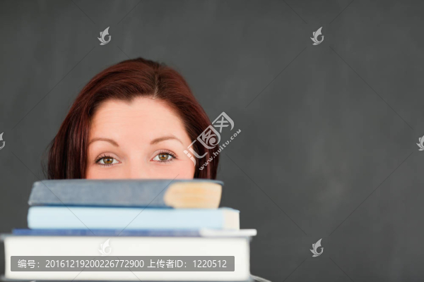 一個(gè)年輕婦女躲在一堆書后面
