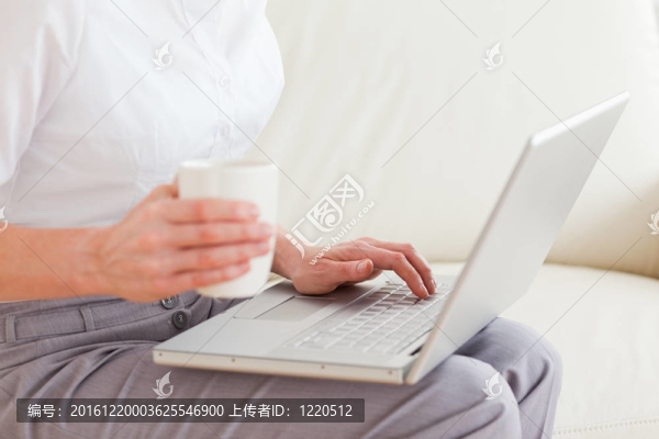 一個(gè)抱著杯子的女人在她的膝上放著一本筆記本