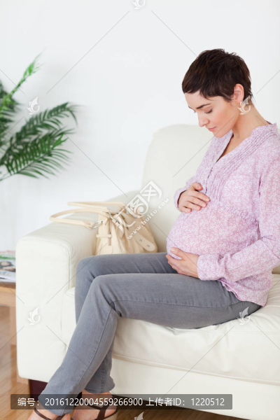 黑色的短頭發(fā)的孕婦坐在沙發(fā)上撫摸她的肚子在候車室
