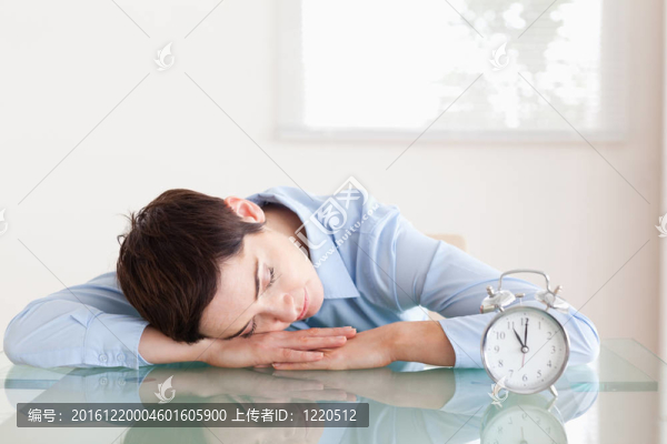 睡眠短頭發(fā)的女人，她的頭靠在桌子旁邊的辦公室里的鬧鐘