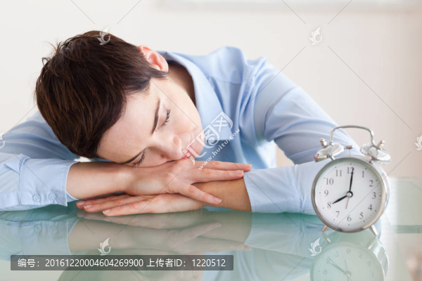 睡的女人，她的頭靠在桌子旁邊的鬧鐘