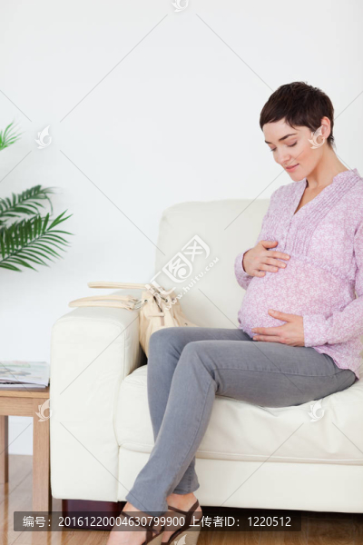 微笑孕婦坐在沙發(fā)上摸她的肚子