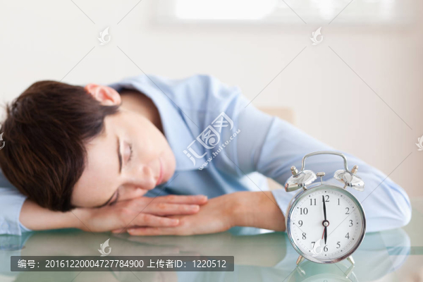沉睡的黑發(fā)女人把頭靠在桌子旁邊的辦公室里的鬧鐘