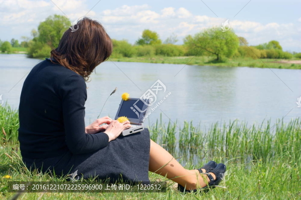 在草地外面的筆記本上打字的女人