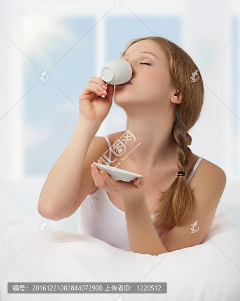年輕漂亮的女人在床上喝咖啡