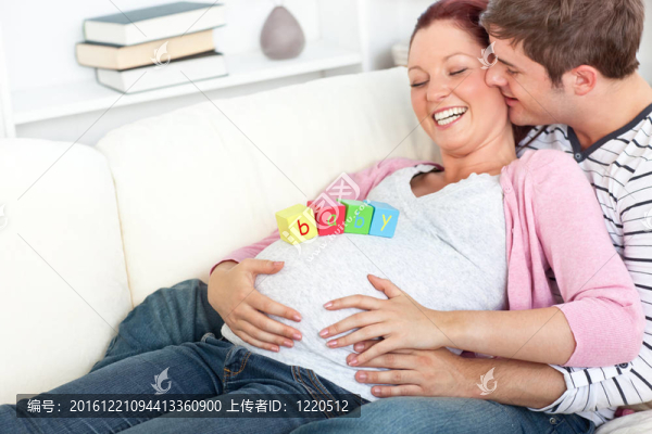 一個(gè)快樂(lè)的孕婦的畫像，她的肚子上有嬰兒立方體，丈夫在沙發(fā)上親吻她