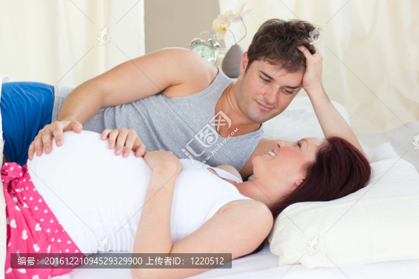 高興的白人孕婦躺在床上與她的丈夫在臥室