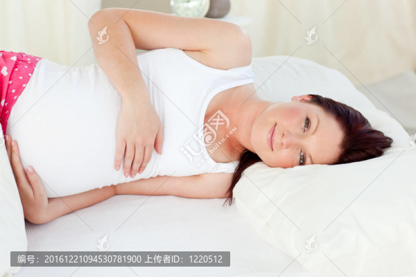 一個(gè)可愛(ài)的孕婦躺在床上，觸摸她的腹部在家里的肖像