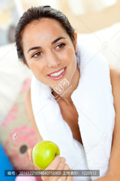 運動的西班牙裔婦女用毛巾在客廳的沙發(fā)上拿著一個蘋果