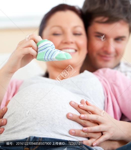 一個孕婦抱著嬰兒鞋和丈夫在家沙發(fā)上的肖像