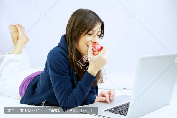 女人微笑著吃蘋果在電腦前躺在床上