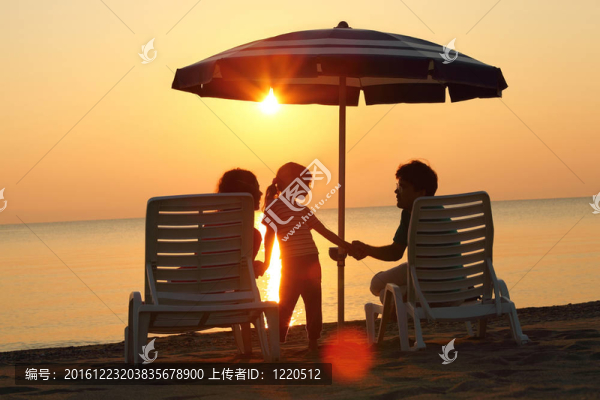 母親和父親坐在海灘上的雨傘下