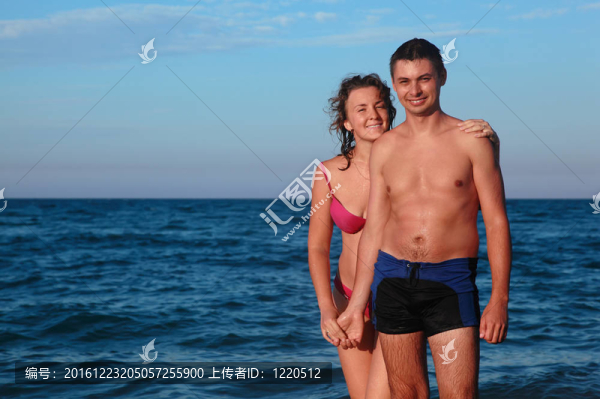 穿著泳衣的男人和女人站在水里，在日落的手