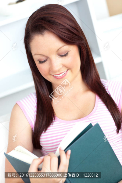 幸福的年輕女人讀著一本書坐在沙發(fā)上