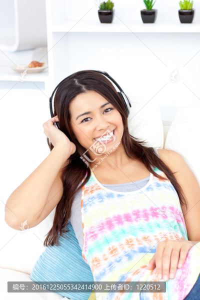 容光煥發(fā)的亞洲年輕女子在沙發(fā)上用耳機聽音樂微笑著拍照