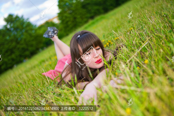 紅色的無袖短上衣的漂亮女孩躺在綠色的草地上