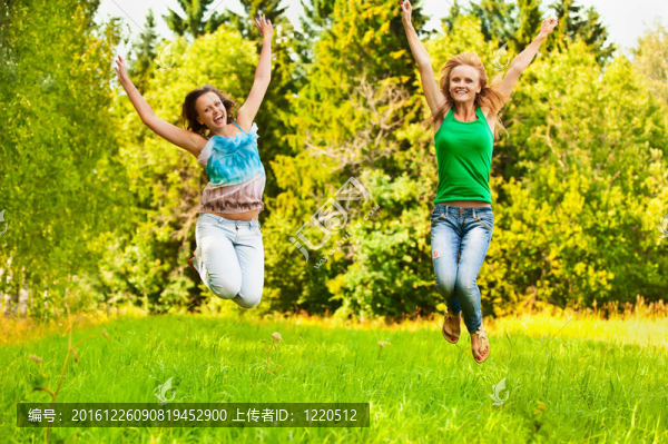 兩個(gè)年輕漂亮的女孩在夏天的綠色公園跳起來(lái)