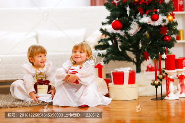 兩個快樂的雙胞胎女孩坐在圣誕樹附近的禮品盒