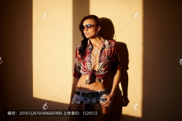 美麗時尚性感的黑人女孩穿著牛仔褲和五顏六色的襯衫在眼鏡后面的日落室內肖像