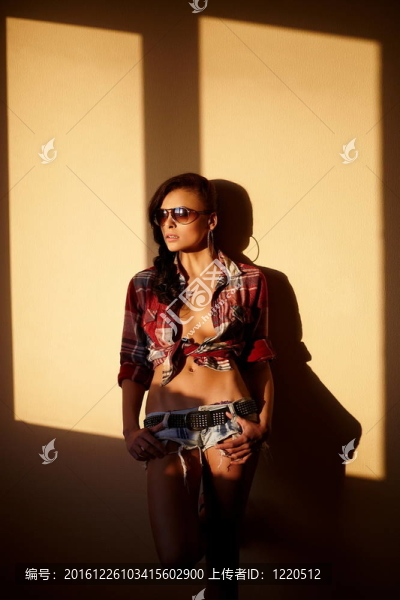 美麗時尚性感的黑人女孩穿著牛仔褲和五顏六色的襯衫在眼鏡后面的日落室內(nèi)肖像