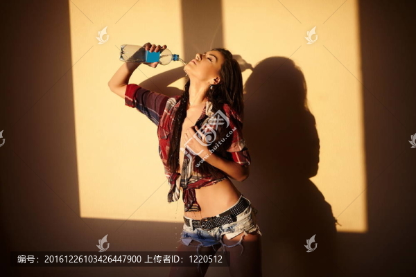 美麗的黑發(fā)女孩肖像時(shí)尚性感的牛仔褲和顏色鮮艷的襯衫和一瓶水在背后的日落