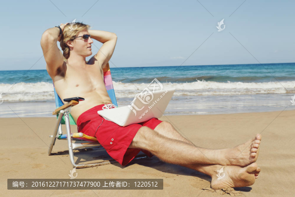年輕迷人的男子在海灘上放松與手機(jī)和C