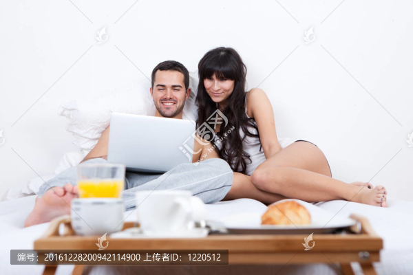 年輕夫婦躺在床上用筆記本電腦