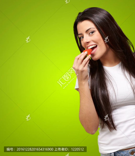 年輕婦女在綠色背景下吃草莓的肖像