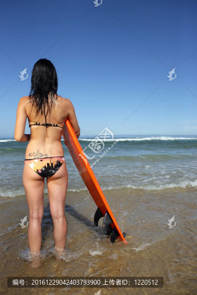 黑發(fā)女人站在海灘上的沖浪板