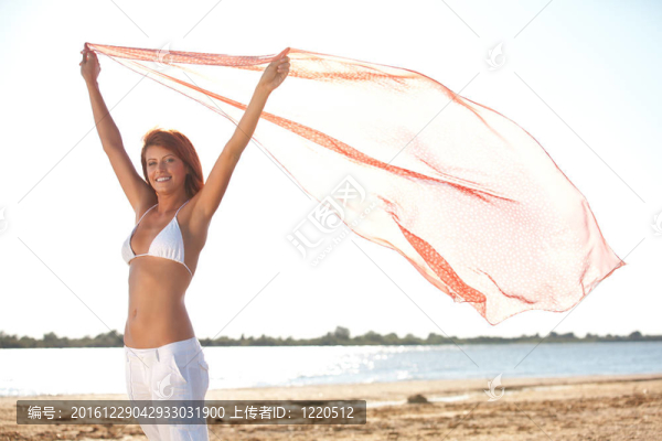 快樂的年輕女子在海灘上拿圍巾