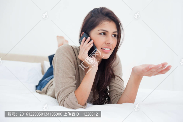 一個(gè)女人伸出她的手；她的雙腿交叉，打電話躺在床上。