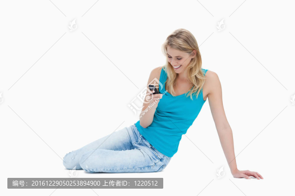 一個(gè)面帶微笑的女人坐在地板上，手里拿著手機(jī)