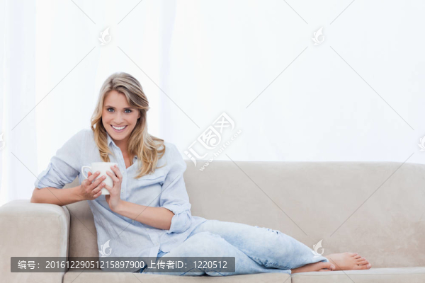 一個(gè)女人拿著一杯咖啡坐在沙發(fā)上