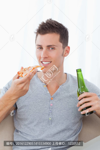 一個微笑的人一手拿披薩和啤酒坐在超視距
