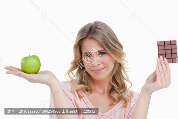 年輕的金發(fā)女人拿著一個蘋果和一塊巧克力