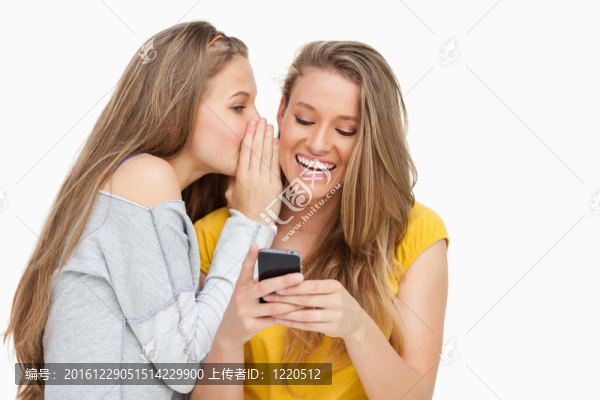 年輕的女人對在電話上發(fā)短信的朋友耳語