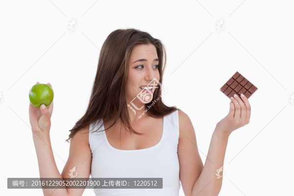 年輕的黑發(fā)女子拿著一塊巧克力和一個蘋果