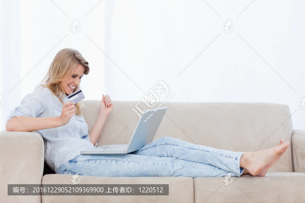 一個興奮的女人拿著銀行卡在她的腿上有一臺筆記本電腦