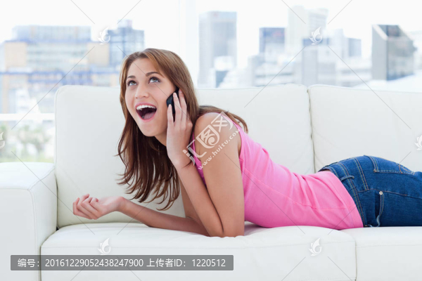 一個(gè)十幾歲的女孩躺在白色沙發(fā)上享受她的電話